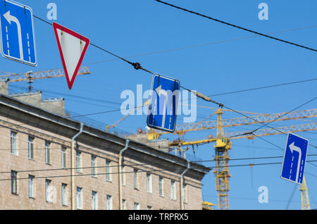 Segnaletica stradale 'girare a sinistra " e " dare modo' in background gru edili e cielo blu Foto Stock