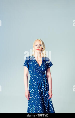 Ritratto in studio di bella donna bionda in un blu scuro abito bianco contro sfondo semplice Foto Stock