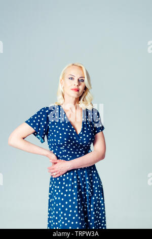 Ritratto in studio di bella donna bionda in un blu scuro abito bianco contro sfondo semplice Foto Stock