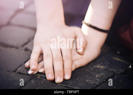 Una mano d'uomo con cura e amore copre una donna di mano, appoggiati sulla pavimentazione di pietra, illuminata dal sole di sera Foto Stock