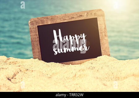 Estate felice scritto su una lavagna vintage nella sabbia di una spiaggia Foto Stock