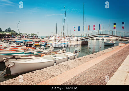 Barche a motore in un piccolo porto di Bardolino con bandiere internazionali Foto Stock