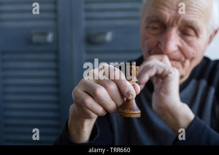 Il vecchio uomo tiene nelle sue mani il pezzo degli scacchi del re, il concetto di vincere o perdere, copyspace Foto Stock