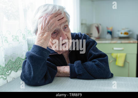 Frustrati grey-haired vecchia donna seduta a casa a tavola. Foto Stock