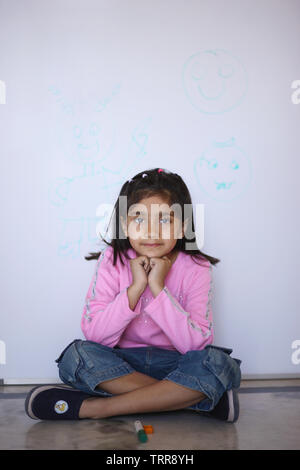 Portrait of a girl sitting on floor in front of a whiteboard Stock Photo