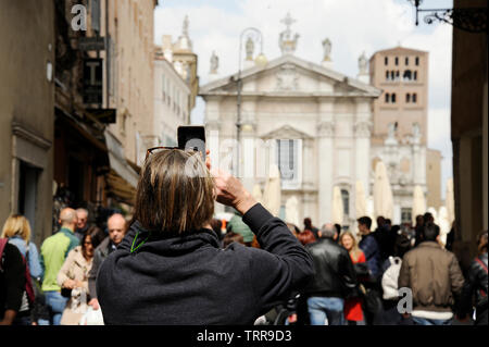 Primo piano del turista uomo sulla strada a Mantova, prendendo foto di Piazza Sordello con il telefono. Mantova, Italia Foto Stock