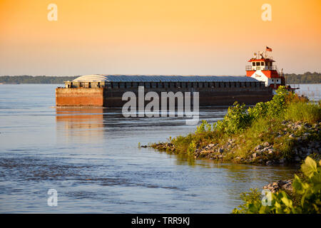 Vista dalla riva di una chiatta caricato la navigazione il possente Fiume Mississippi con l aiuto di un rimorchiatore al tramonto vicino a Greenville, Mississippi Foto Stock