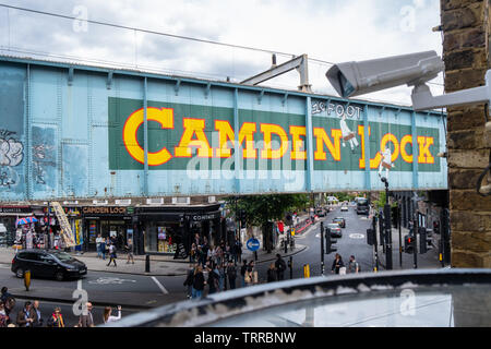 Sicurezza telecamera TVCC in primo piano che si affaccia sul mercato di Camden e iconico dipinto di Camden Lock segno sul lato del ponte ferroviario a Londra con street Foto Stock