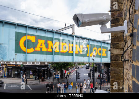 Sicurezza telecamera TVCC affacciato sul mercato di Camden e iconico dipinto di Camden Lock segno sul lato del ponte ferroviario a Londra con street e persone in Foto Stock