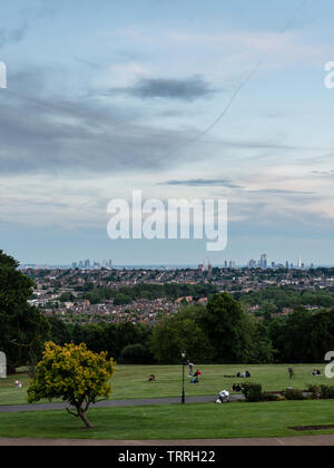 London, England, Regno Unito - 1 Giugno 2019: persone sedersi in Alexandra Palace parco come tramonto cade sui pascoli e sullo skyline di Londra. Foto Stock