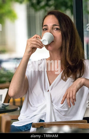 Ritratto di una donna di bere una tazza di caffè espresso seduti all'aperto. Foto Stock