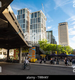 London, England, Regno Unito - 31 Maggio 2019: un ciclista passa il caffè all'aperto della London South Bank Centre, con costruire nuovi edifici appartamento sotto con Foto Stock