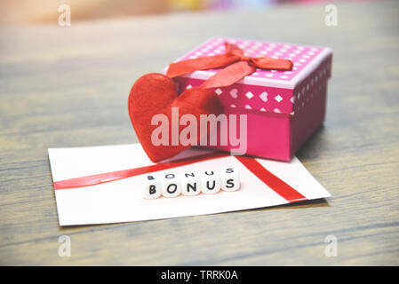 Bonus annuale concetto / bonus carta nella busta di carta con confezione regalo sorpresa e cuore rosso per incoraggiamento morale nella tabella office company Foto Stock