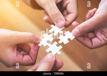Primo piano immagine di molte persone mani e mettere un pezzo di bianco puzzle insieme Foto Stock