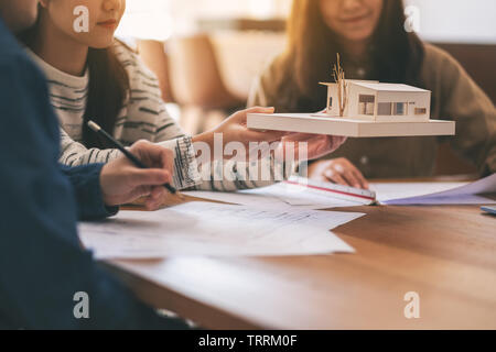 Gruppo di un architetto holding e discutere di un modello di architettura con disegno del negozio di carta sul tavolo in ufficio Foto Stock