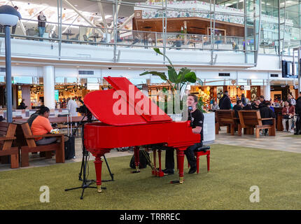 Musicista che gioca su una rossa pianoforte presso l'Aeroporto di Brisbane all'area partenze, Queensland, QLD, Australia Foto Stock