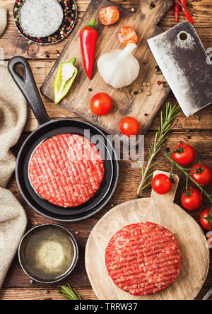 Crudo fresco sminuzzato in casa gli agricoltori grill hamburger di manzo sul round tagliere e padella con le spezie e le erbe aromatiche e le carni hatchet su legno. Foto Stock