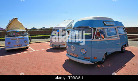 Tre Classico Volkswagen camper parcheggiato insieme con la spiaggia di capanne in background. Foto Stock