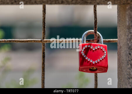 Lucchetto rosso con un hart forma realizzato in piccoli cristalli appesi bloccato sulla staccionata che simboleggia l'amore. Foto Stock