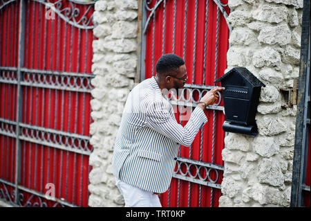 Ricca e di stile americano africano uomo in blazer e occhiali controllare la sua casella postale all'aperto nel recinto. Foto Stock
