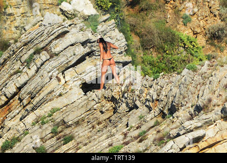 Una donna che cammina su di una scogliera rocciosa su Sveti Nikola isola nei pressi di Budva, Montenegro. Foto Stock