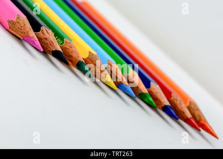 In piedi fuori dalla folla del concetto. Mazzetto assortiti di multi matite colorate matite colorate a disposizione arcobaleno su sfondo bianco, piatto laici. Geometria pa Foto Stock