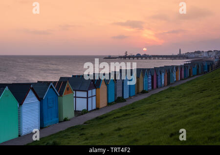 Pittoresca spiaggia di capanne sulla Herne Bay Seafront come il sole sorge sulla storica Pier. Foto Stock