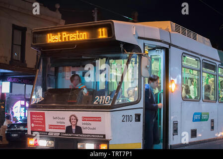 Una persona di sbarco (getting off) un moderno Melbourne il tram in direzione ovest Preston su Brunswick Street, Fitzroy in Victoria, Australia di notte Foto Stock