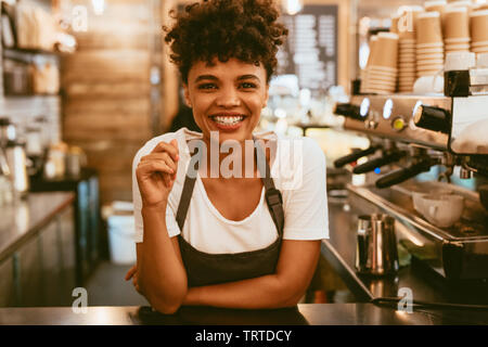 Sorridente giovane donna in grembiule permanente al coffee shop counter. Fiducioso barista femmina in piedi dietro il contatore.
