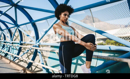 Montare la giovane donna stretching la sua gamba dopo una corsa in città. Donna africana in sportswear preparando per l'esecuzione di allenamento. Foto Stock
