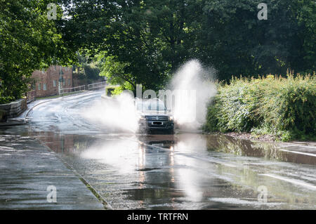 Intorno al Regno Unito - una vettura VW schizzi attraverso una strada allagata in tipico British Estate Meteo! Una sequenza di tre immagini sono disponibili. Foto Stock