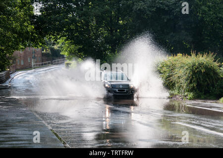 Intorno al Regno Unito - una vettura VW schizzi attraverso una strada allagata in tipico British Estate Meteo! Una sequenza di tre immagini sono disponibili. Foto Stock