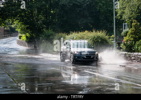 Intorno al Regno Unito - una vettura VW schizzi attraverso una strada allagata in tipico British Estate Meteo! Una sequenza di tre immagini sono disponibili. Foto Stock