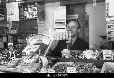 Degli anni Cinquanta, foto storiche che mostra un maschio dolce negozio proprietario dietro il bancone, Inghilterra, Regno Unito. Foto Stock