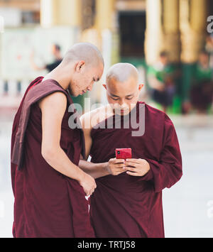 Yangon, Myanmar - Marzo 2019: giovane buddista novizio monaci con i gadget in Shwedagon pagoda tempio complesso. Cerca sulla schermata telefono. Foto Stock