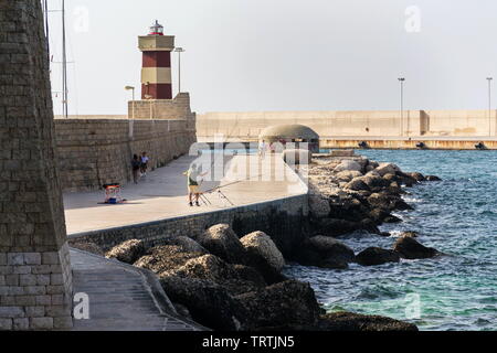 MONOPOLI, Italia - 6 Luglio 2018: uomo pesca nella parte anteriore del faro nel porto di Monopoli vicino al Castello di Carlo V il 6 luglio 2018 a Monopoli, Italia. Foto Stock