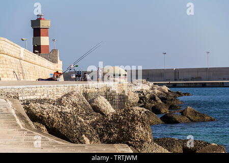 MONOPOLI, Italia - 6 Luglio 2018: uomo pesca nella parte anteriore del faro nel porto di Monopoli vicino al Castello di Carlo V il 6 luglio 2018 a Monopoli, Italia. Foto Stock