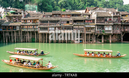 2 giugno 2019, Fenghuang Cina : tradizionali barche di legno pieno di turisti crusing sul fiume Tuojiang e vecchie case tradizionali su riverside in Fenghuan Foto Stock