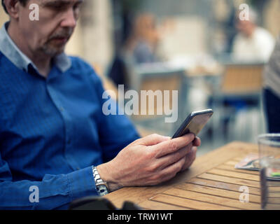Uomo adulto con blue chemise seduto in un bar texting lo smartphone Foto Stock