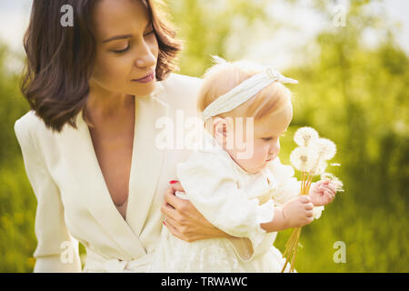 Outdoor fashion Ritratto di giovane madre bella e poco carino figlia soffiando di tarassaco sul prato verde. Immagine a molla Foto Stock