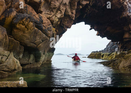 Kayak di mare attraverso un arco naturale intorno al Summer Isles, Wester Ross, altopiani, Scozia Foto Stock