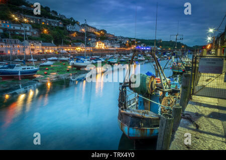 Dopo un altro freddo nuvoloso giorno le luci sfarfallio su come la luce del giorno dà modo al crepuscolo nello storico porto di pesca di Looe in Cornovaglia. Foto Stock