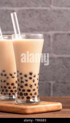 Popolare bevanda Taiwan - Bubble latte tè con tapioca pearl palla nel bicchiere e paglia, tavolo in legno grigio Sfondo mattone, close up, spazio di copia Foto Stock