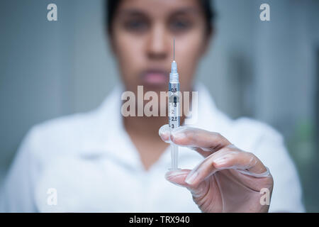 Medicazione femmina infermiera con un volto minaccioso e vaccino di contenimento shot in mano per terrorizzare la paziente. Foto Stock