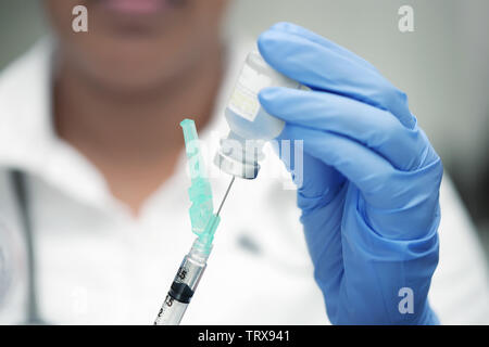 Medico professionista con il bianco scrubs e guanti in nitrile blu, la preparazione di un vaccino shot. Foto Stock