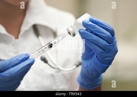 Farmaco infermiera indossare guanti protettivi e bianco scrubs ottenere un ago o shot pronto per l'iniezione. Foto Stock