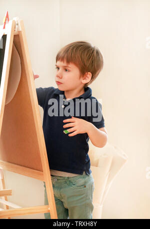 Il bambino è il disegno e la pittura con il pennarello su carta del disegno di legno artista scheda cavalletto per ragazzi e bambini a casa. Infanzia. Carino piccolo ragazzo. Foto Stock