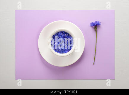 Layout creativo fatto di blu petali di fiordaliso galleggianti in acqua sulla luce Pastello Lilla posa di sfondo sulla tabella grigia.Piana, laici concetto. Foto Stock