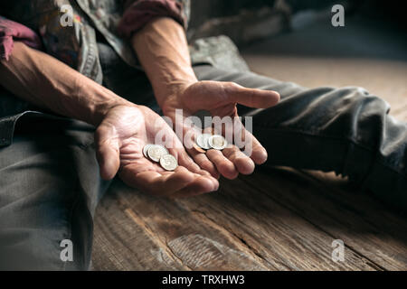 Mendicante maschio le mani in cerca di denaro, monete dalla gentilezza umana su pavimento di legno alla pubblica strada o lungo la strada pedonale. Senzatetto poveri della città. Problemi con la finanza, luogo di residenza. Foto Stock