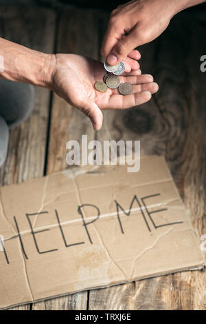 Mendicante maschio le mani in cerca di denaro con segno HELP ME da gentilezza umana su pavimento di legno alla pubblica strada o lungo la strada pedonale. Senzatetto poveri della città. Problemi con la finanza, luogo di residenza. Foto Stock